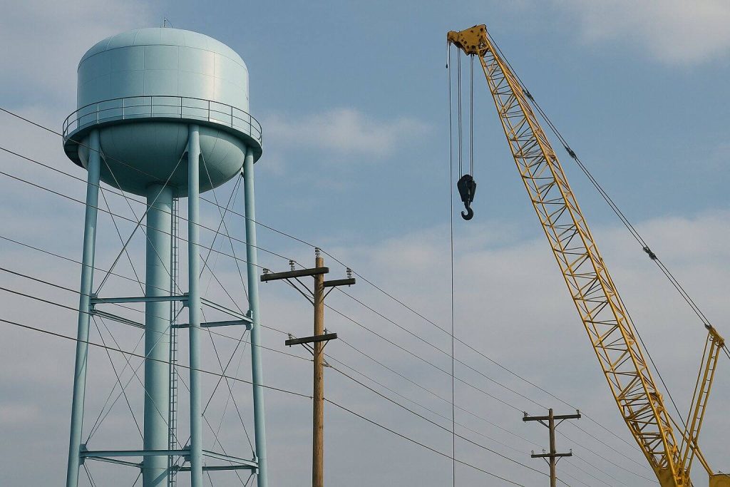 Trabalho em altura próximo a rede elétrica, com guindaste e reservatório elevado, exemplificando atividades que exigem aplicação da NR 35